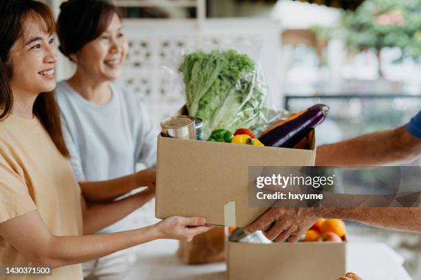 female volunteers giving free groceries to elderly person at food bank - food security stock pictures, royalty-free photos & images
