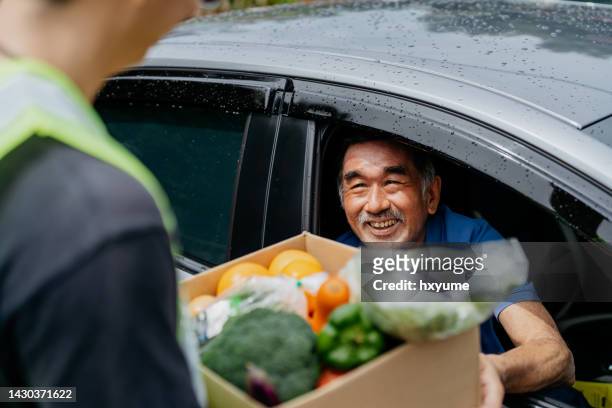asian senior man receiving donated groceries from volunteer at drive through food bank - charity box stock pictures, royalty-free photos & images