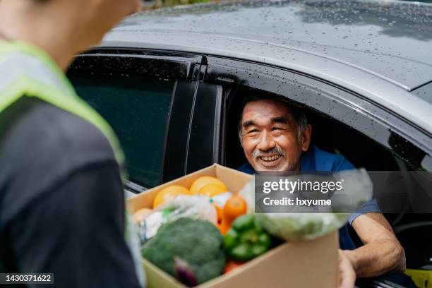asian senior man receiving donated groceries from volunteer at drive through food bank - banco alimentar imagens e fotografias de stock