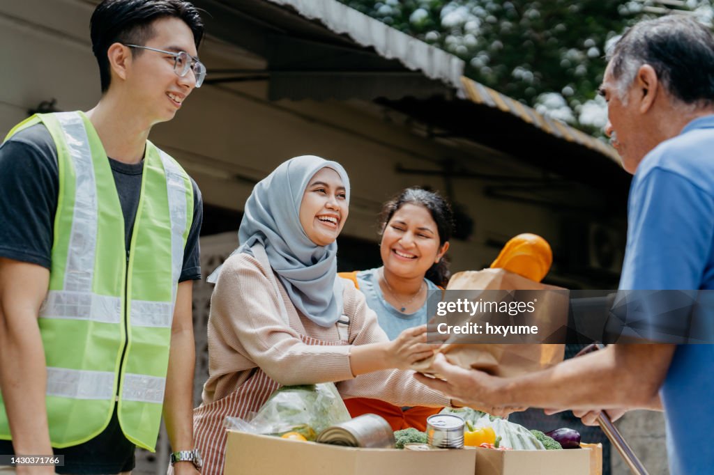 Female volunteers giving free food to elderly person at food bank