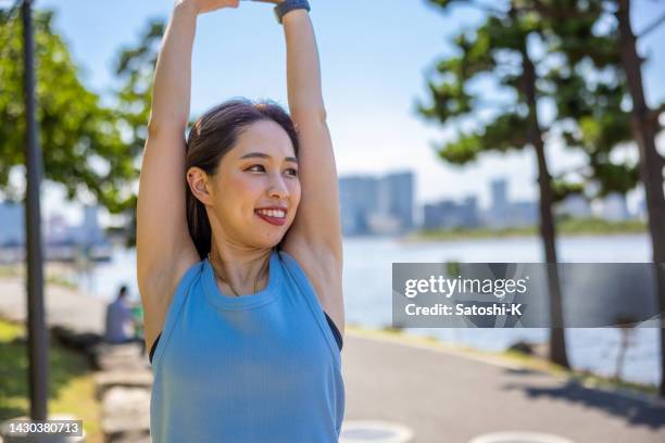 female athlete stretching in public park - sleeveless stock pictures, royalty-free photos & images