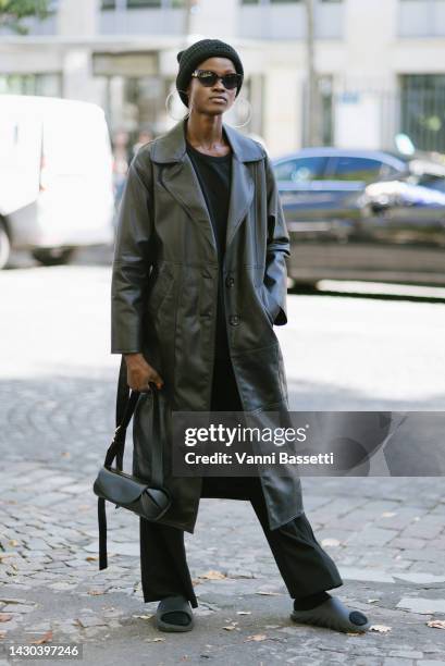 Model poses wearing a black beanie, a black leather coat, Jil Sander cannolo black leather bag and Adidas Yeezy slides after the Miu Miu show at the...