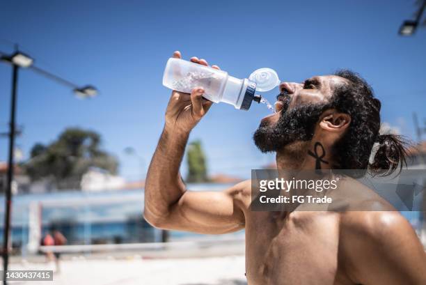 homem bebendo água em uma quadra de vôlei de praia - sedento - fotografias e filmes do acervo