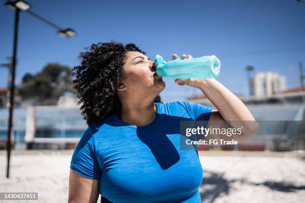 mulher que bebe água em uma quadra de vôlei de praia - sedento - fotografias e filmes do acervo