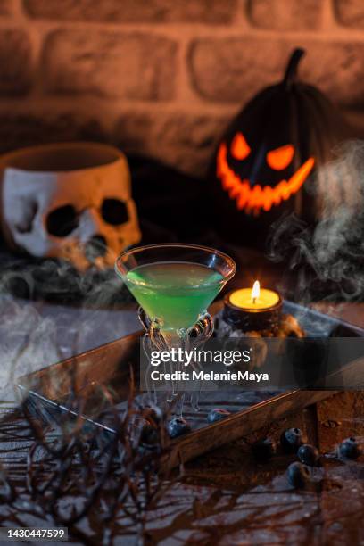 green spooky halloween cocktail drink in dark kitchen with fog, skull and pumpkin jack o’ lantern - german greens party stock pictures, royalty-free photos & images