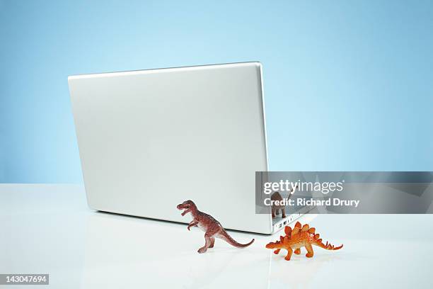 toy dinosaurs emerging from laptop - toy dinosaur fotografías e imágenes de stock