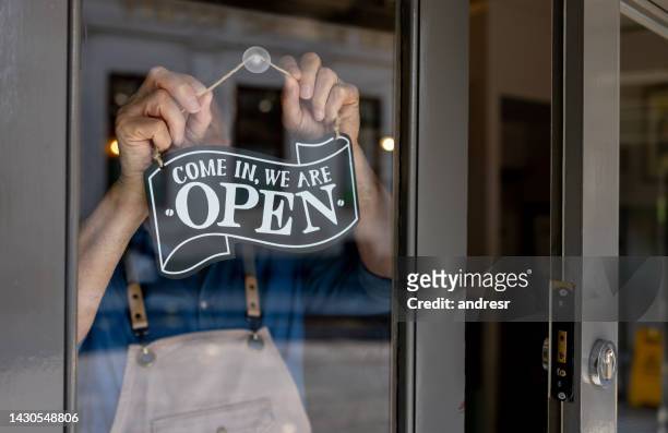 primer plano del dueño de un negocio colgando un letrero abierto en la puerta de su restaurante - cultura británica fotografías e imágenes de stock