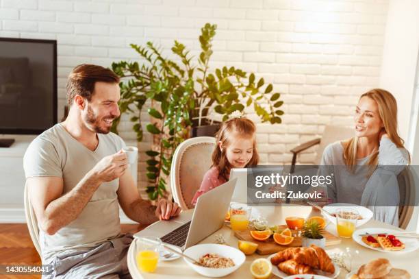 junge glückliche familie frühstückt und nutzt moderne technologie - kirschen tisch weiß stock-fotos und bilder