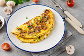 Omelet with fried mushrooms and fresh herbs in a plate on a concrete background. Delicious healthy breakfast. Top view. Copy space.