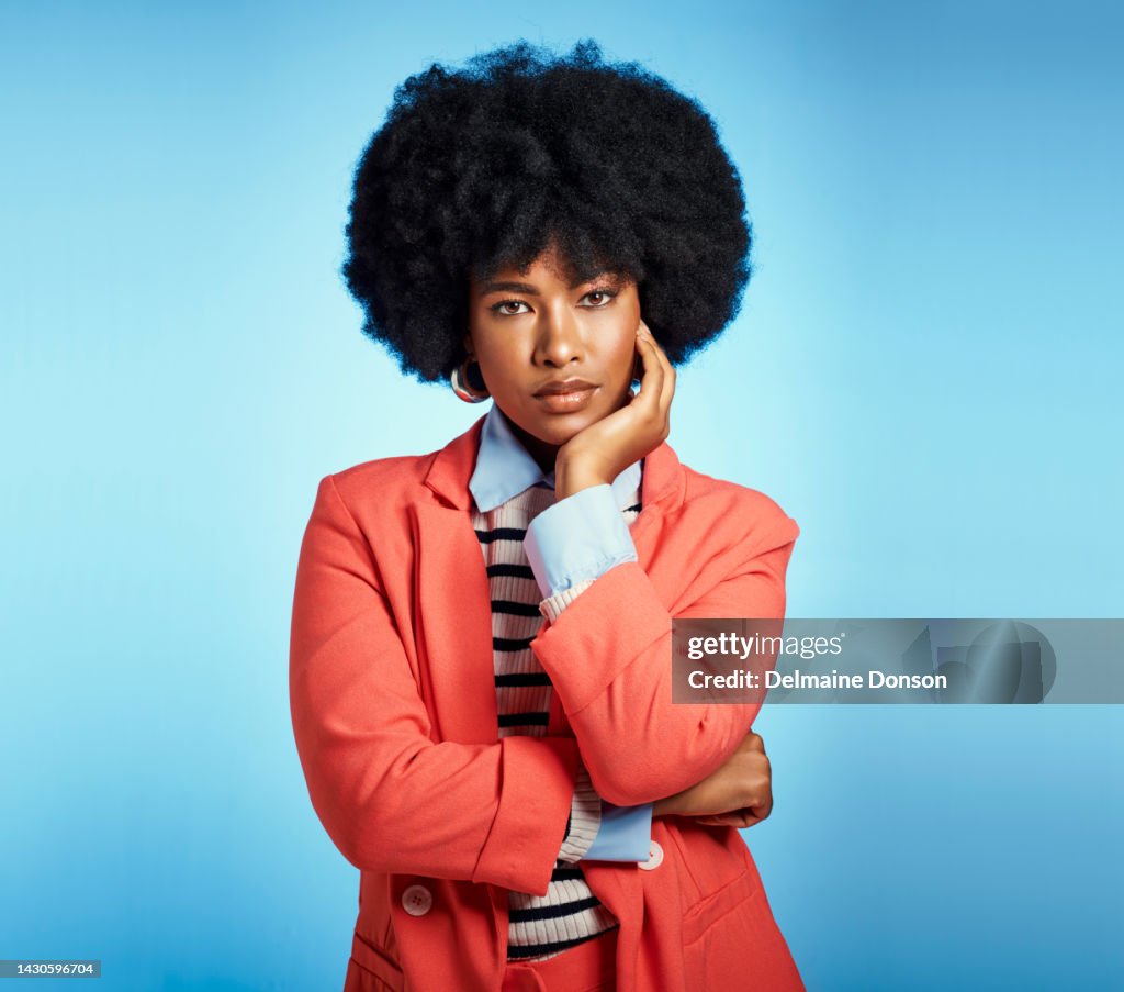 Stylish, fashion and serious black woman with an afro and beautiful face while standing against a blue studio background. Portrait of an African female feeling confident in a smart casual suit
