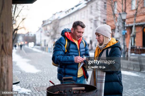 paar an einem marktstand mit frisch gerösteter kastanie in der stadt im winter - maroni stock-fotos und bilder