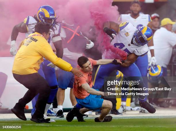 Fan with a smoke bomb is tackled on the field by Los Angeles Rams' Bobby Wagner, #45 Takkarist McKinley and a security guard during their NFL game...