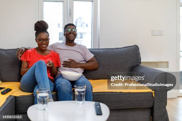 a happy african couple is watching a tv in the living room. - reportage home stock pictures, royalty-free photos & images