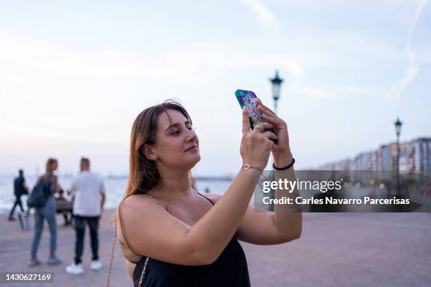 young woman looks at cell phone while smiling - taken on mobile device stock pictures, royalty-free photos & images