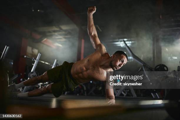 muscular build man exercising endurance in one-hand plank position in a gym. - man muscular build stock pictures, royalty-free photos & images