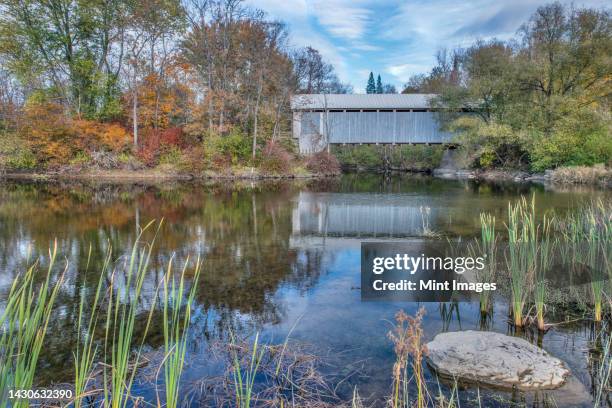 a covered bridge across a river in autumn - eastern townships quebec stock pictures, royalty-free photos & images
