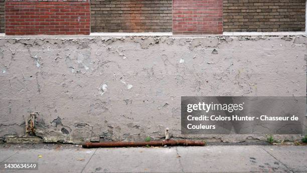 painted and weathered cement and brick wall with a rusty metal tube on the pavement in montreal, qc, canada - ugly wallpaper stock pictures, royalty-free photos & images