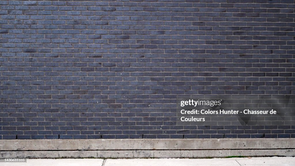 Empty and weathered dark gray brick wall and cement sidewalk in Montreal, Qc, Canada