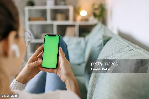 young woman using phone with green screen while relaxing on the sofa - chroma key stock pictures, royalty-free photos & images