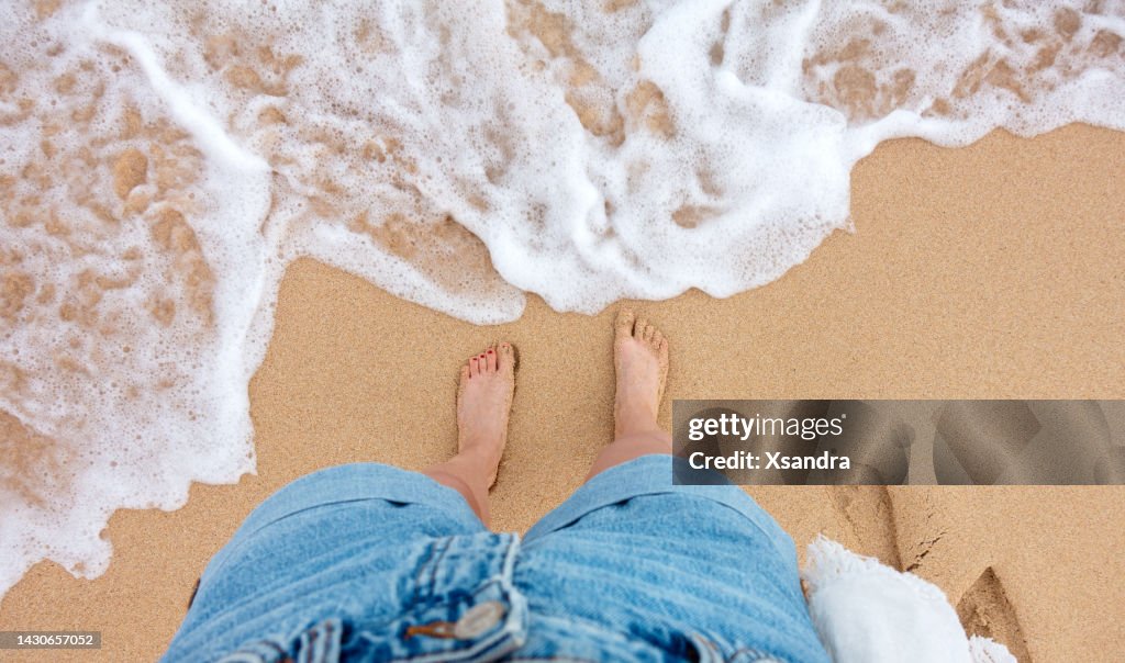 POV de mujer joven de pie en la playa de arena