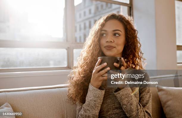 young woman on sofa with mug in living room thinking, relax and happy next to the window. content, lady or girl calm, looking out of window with cup of coffee or tea in apartment or hotel room. - relief emotion stock pictures, royalty-free photos & images