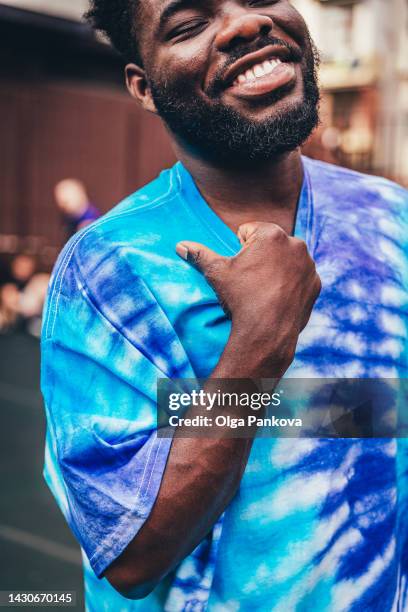 smiling black young man wearing  blue tie-dye t-shirt - tie dye shirt stock pictures, royalty-free photos & images