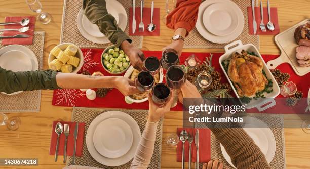 christmas, party and family make toast at table with food at dinner or festive celebration. people, hands and wine celebrate, lift glasses in home together during holiday event and cheers with drink - friends toasting above table stock pictures, royalty-free photos & images