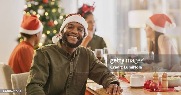 friends at table, christmas and happy man at lunch to celebrate holiday. santa hats, food and wine, eat and drink together. black man at dinner party celebration with family, conversation and smile. - portrait of handsome man stockfoto's en -beelden