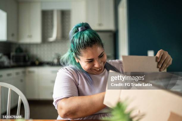 mid adult woman opening cardboard box in the dining room at home - delivery character stock pictures, royalty-free photos & images