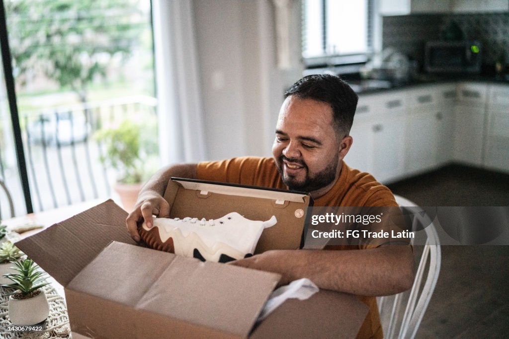 Mid adult man opening package in the dining room at home