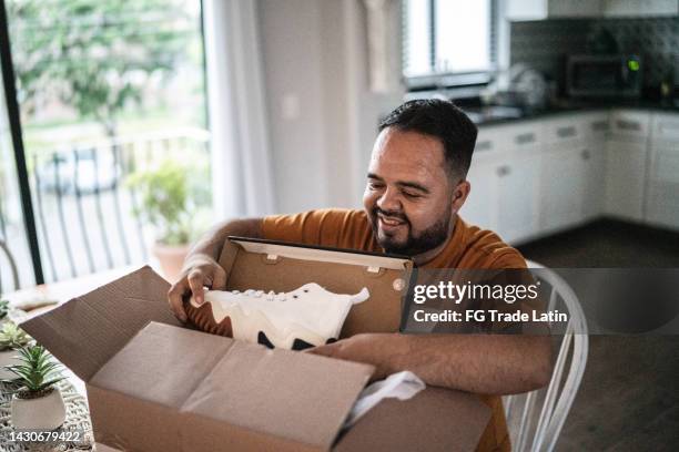 mid adult man opening package in the dining room at home - shoes man stock pictures, royalty-free photos & images