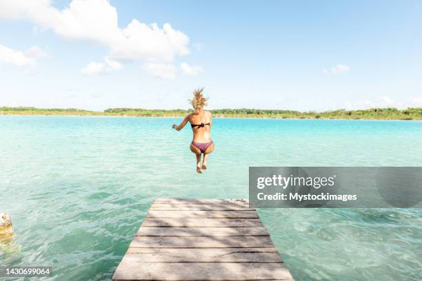 jeune femme heureuse sautant de la jetée dans le magnifique lac - ponton mer photos et images de collection
