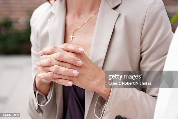 close up of woman's hands folded in prayer - a cross necklace stock-fotos und bilder