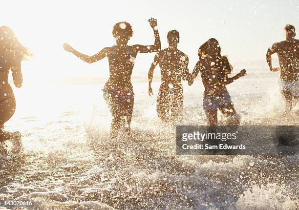 friends playing in waves on beach - beach running bildbanksfoton och bilder