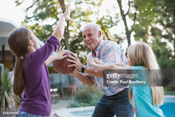 older man playing basketball with granddaughters - blocking sports activity stock pictures, royalty-free photos & images