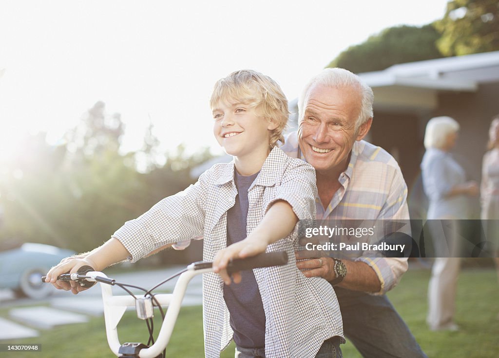 Older man helping grandson ride bicycle