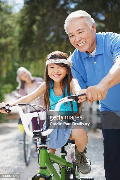 ältere mann helfen enkelin reiten fahrrad - fahrrad fahren großeltern mit kind stock-fotos und bilder