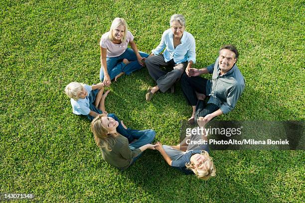 people sitting in circle on grass holding hands looking up at camera - bambini seduti in cerchio foto e immagini stock