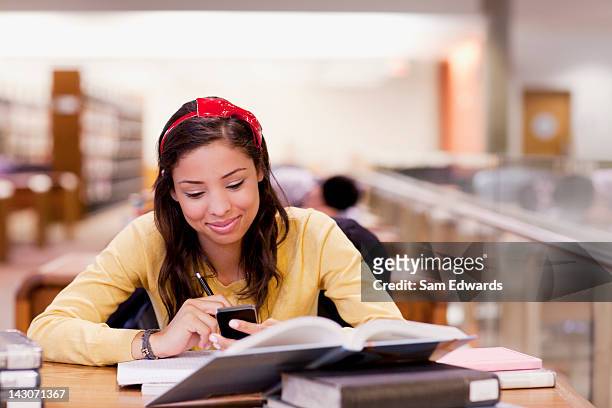 student using cell phone and studying in library - samuser stock pictures, royalty-free photos & images