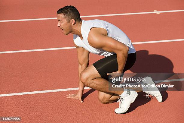 injured runner kneeling on running track - injured runner stock pictures, royalty-free photos & images