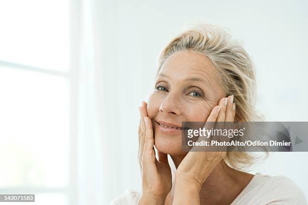 mature woman touching cheeks, smiling, portrait - vrouw 50 jaar stockfoto's en -beelden