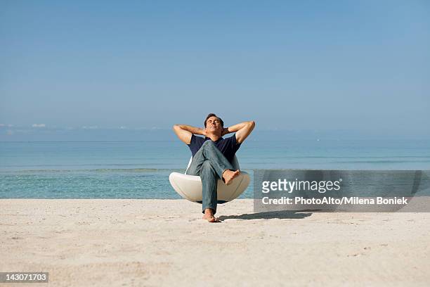mid-adult man relaxing in armchair on beach with eyes closed - mid adult men stock pictures, royalty-free photos & images
