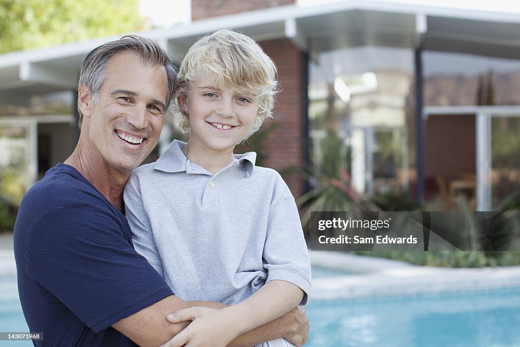 Padre e hijo, que abrazan junto a la piscina
