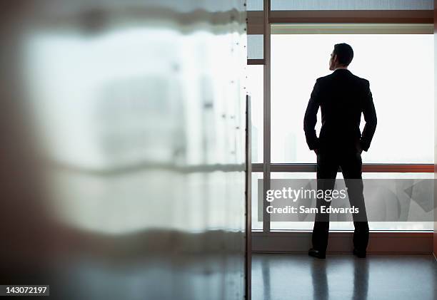 uomo d'affari guardando fuori la finestra ufficio - guardare fuori dalla finestra foto e immagini stock