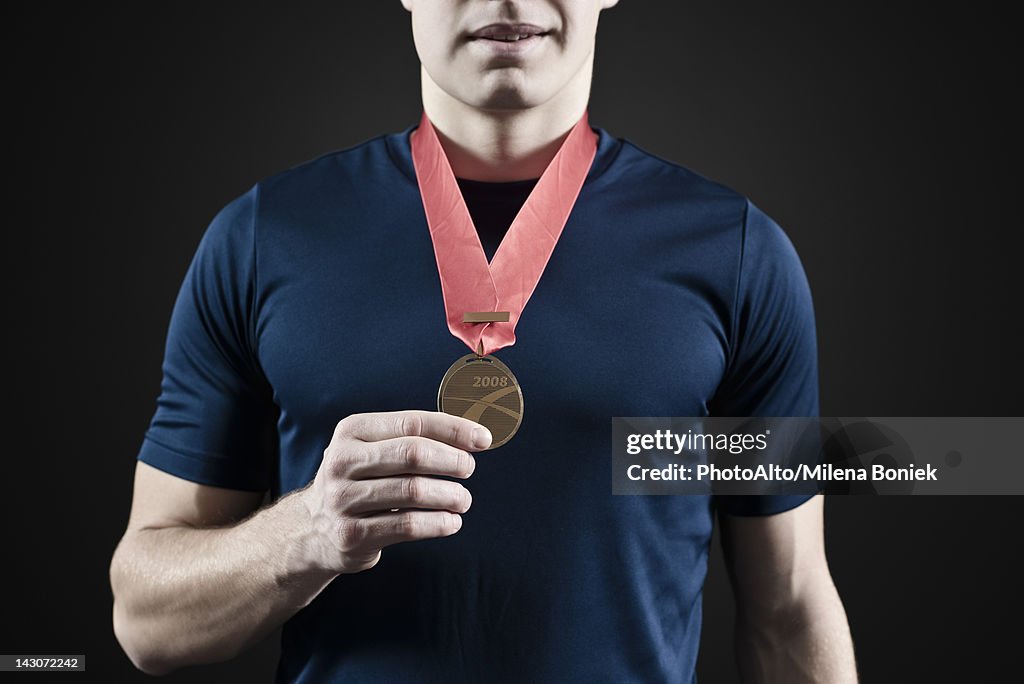 Male athlete holding medal, mid section