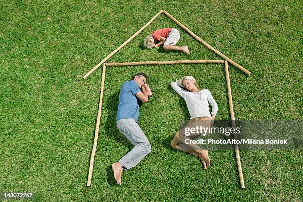 family with one child lying on grass within outline of house, high angle view - position du foetus photos et images de collection