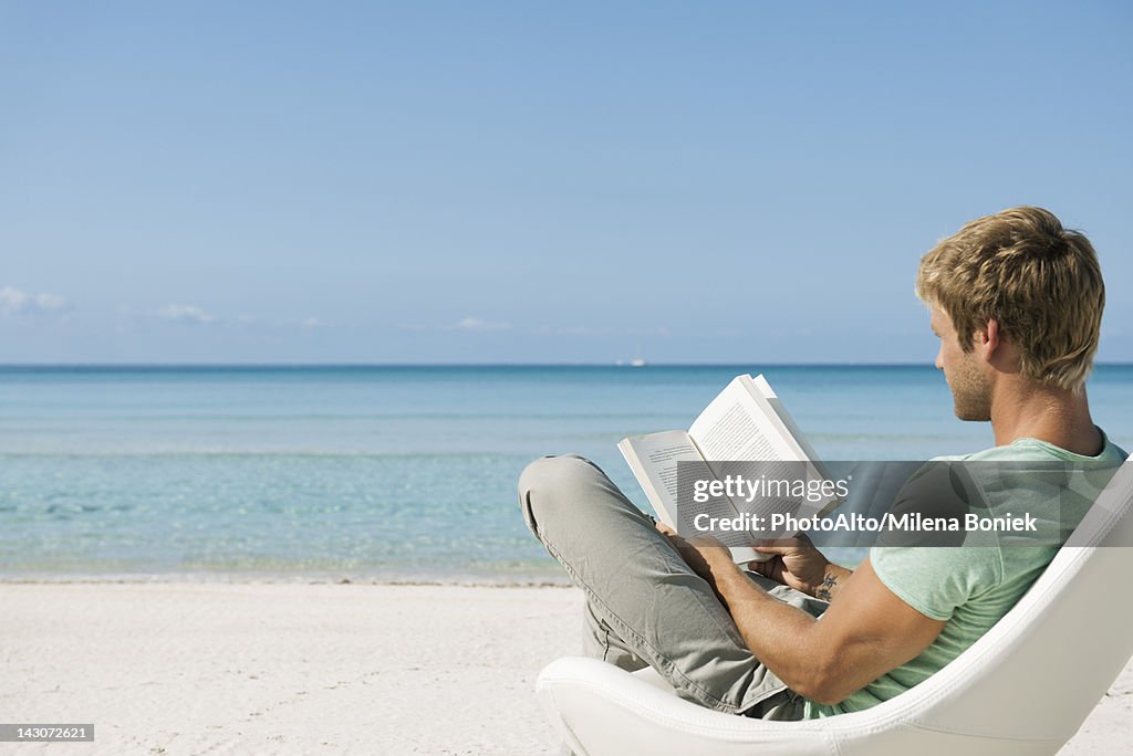 Young man reading book on beach