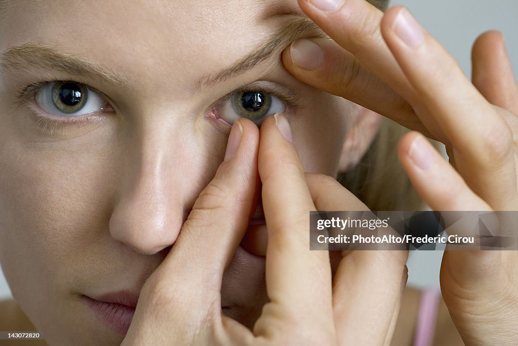 Young woman putting in contact lens