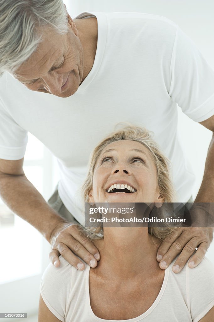 Mature couple smiling at each other as man massages woman's shoulders