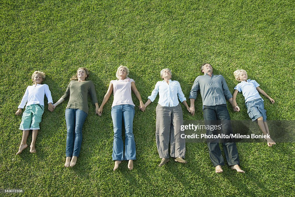 Group lying side by side on grass holding hands